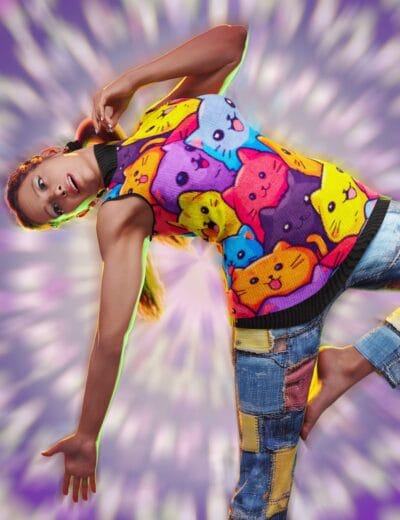 Model in neon cat sweater and patchwork jeans against purple swirl background
