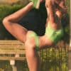 A young woman pausing to stretch while jogging in the park. She has visible stretch marks on her thighs, buttocks and hips.