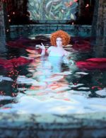 Vivid fantasy female character with curly red hair floating in a mystical pool surrounded by floating red cloth, with a detailed garden and glowing background, showcasing high-quality Daz3D assets.