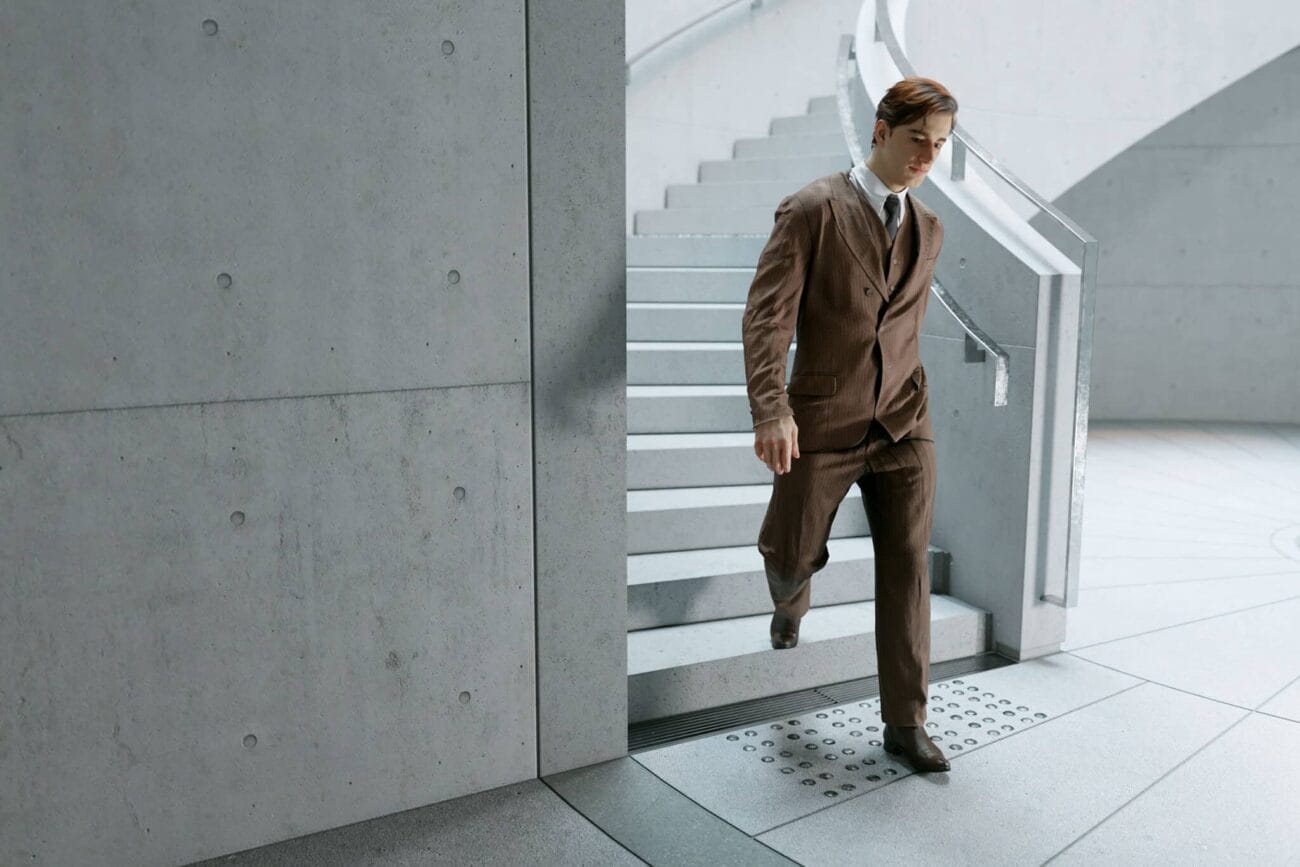 Elegant businessman in a brown suit walking down modern concrete stairs in an urban setting.