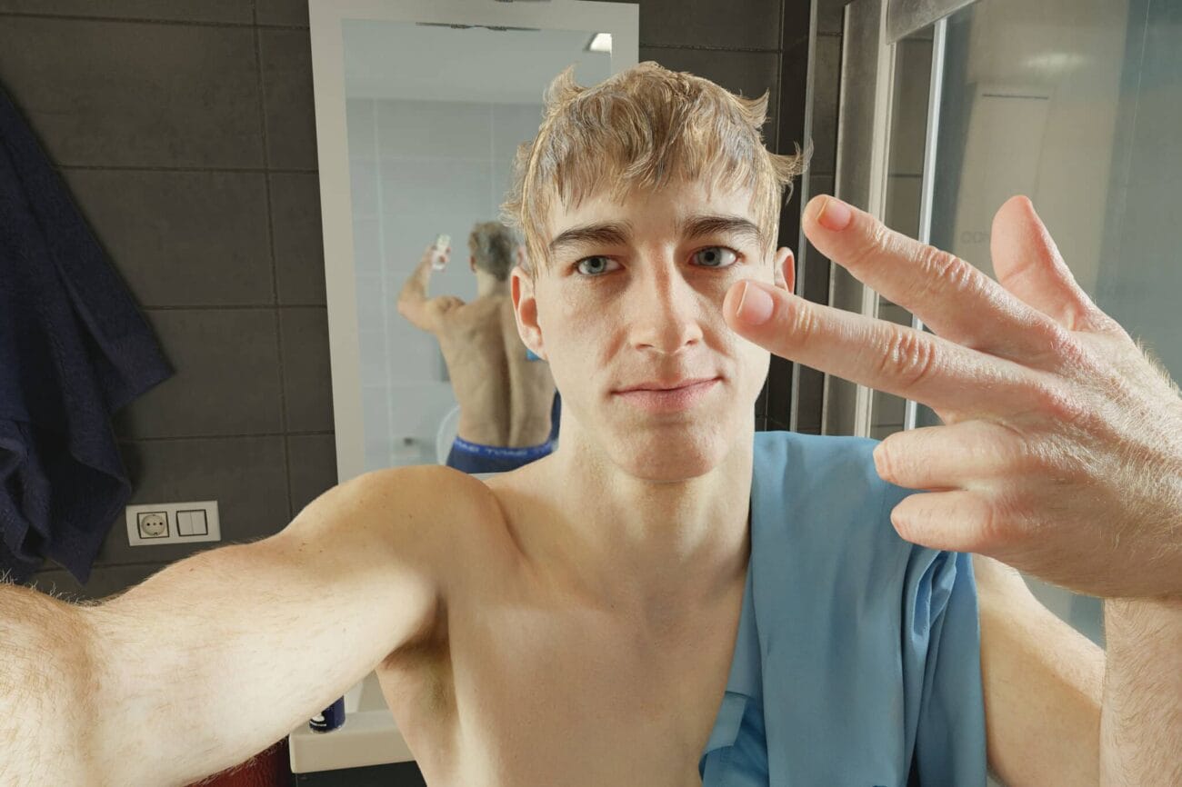 Young man taking a selfie in the bathroom mirror, showing his reflection and casual pose.