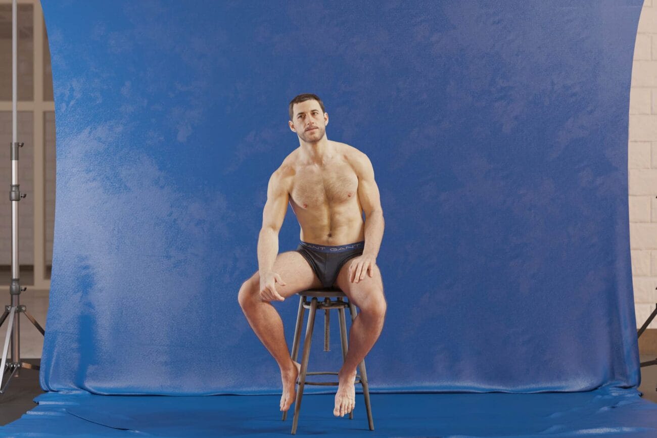 3D male model sitting on a stool in front of a blue photo backdrop for Daz3D assets, showcasing high-quality 3D character design and rendering for digital art projects.