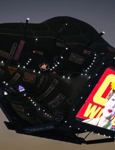 Vivid nighttime shot of a floating digital billboard with city advertisements, featuring a colorful image of a woman with bright makeup on an illuminated screen.